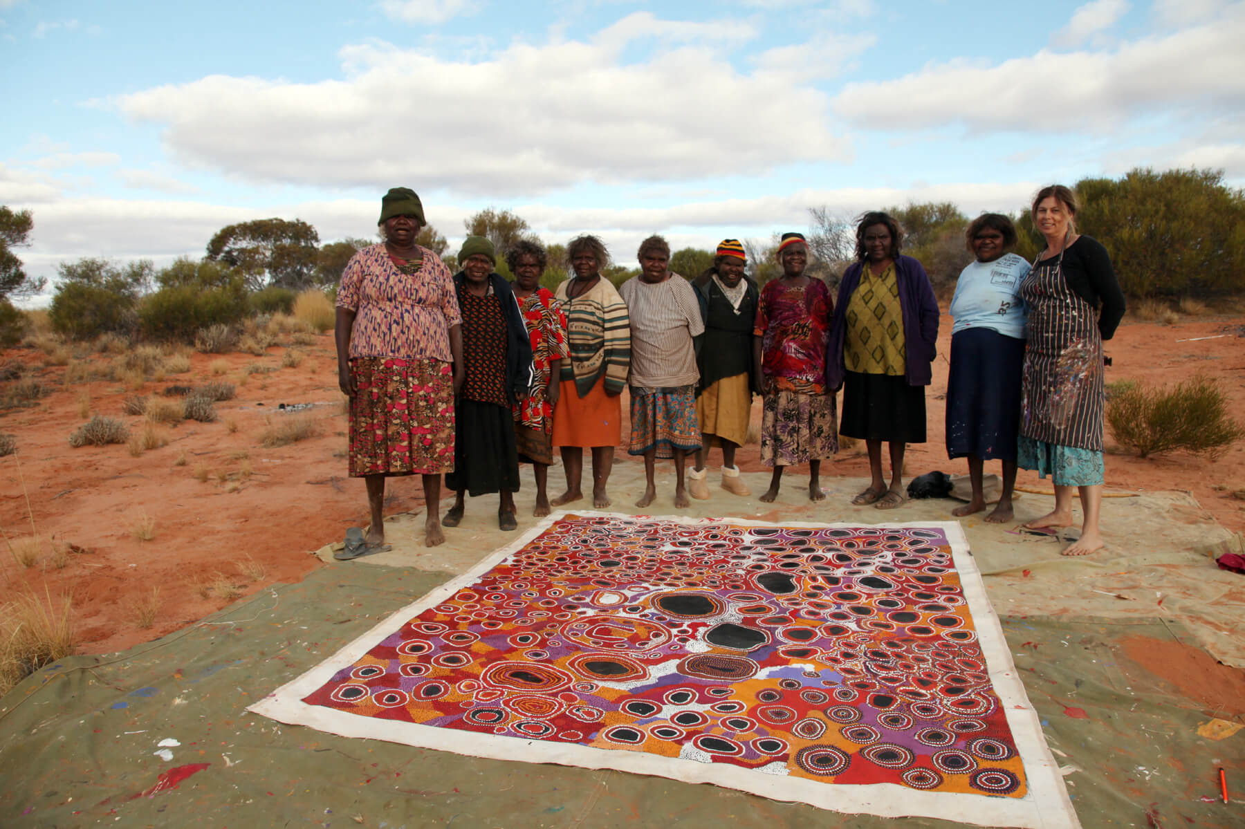 Women from Spinifex Arts standing around a lage colourful canvas showing places of significance.